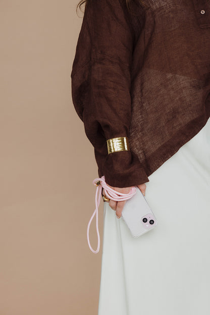 Close-up of a pink Colorful PHONE CORD, phone held against a brown sleeve with a gold cuff bracelet.