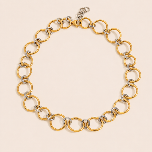 Two-tone Contradiction NECKLACE with linked gold and silver circles forming a chunky chain, laid flat on beige.