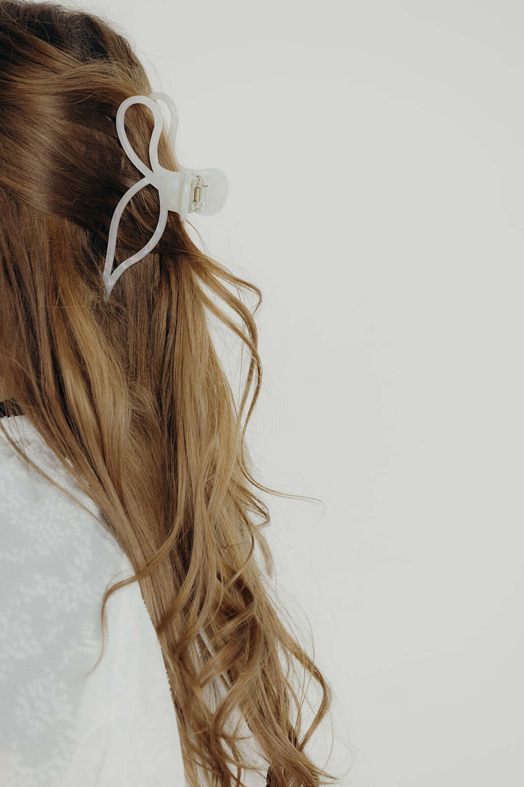 Coquette HAIR CLIP in solid white, worn holding a half-up style on wavy blonde hair, side view.