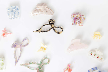 Coquette HAIR CLIP shown among a wide flat-lay assortment of differently shaped acetate hair clips in various colors and patterns.