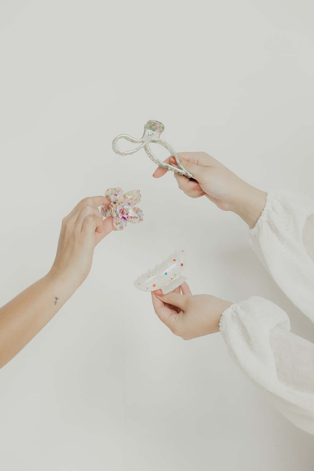Coquette HAIR CLIP held up alongside other differently shaped hair clips, a staged lifestyle shot with two hands.