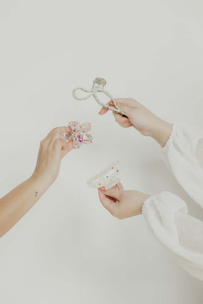 Coquette HAIR CLIP held up alongside other differently shaped hair clips, a staged lifestyle shot with two hands.