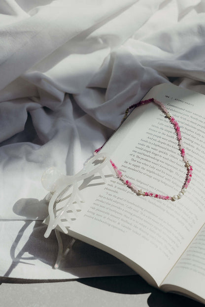 Coquette HAIR CLIP in solid white, styled on an open book with a pink beaded necklace draped across the page.