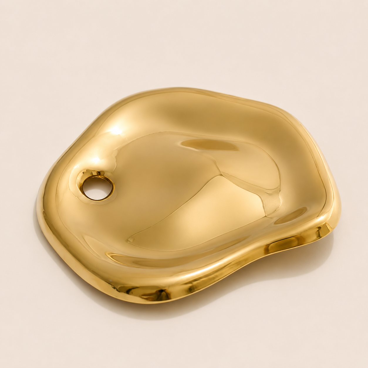 Gold molten pebble-shaped brooch with a rounded pierced detail on a cream backdrop — Folie à Trois Costa BROOCH