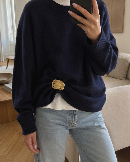 Close-up mirror selfie of a model wearing a gold Costa BROOCH cinching a navy sweater over jeans — Folie à Trois
