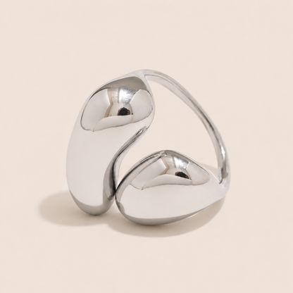 Silver bypass ring with two glossy teardrop-shaped domes wrapping around each other, on a cream backdrop — Folie à Trois Côte d'Été RING.
