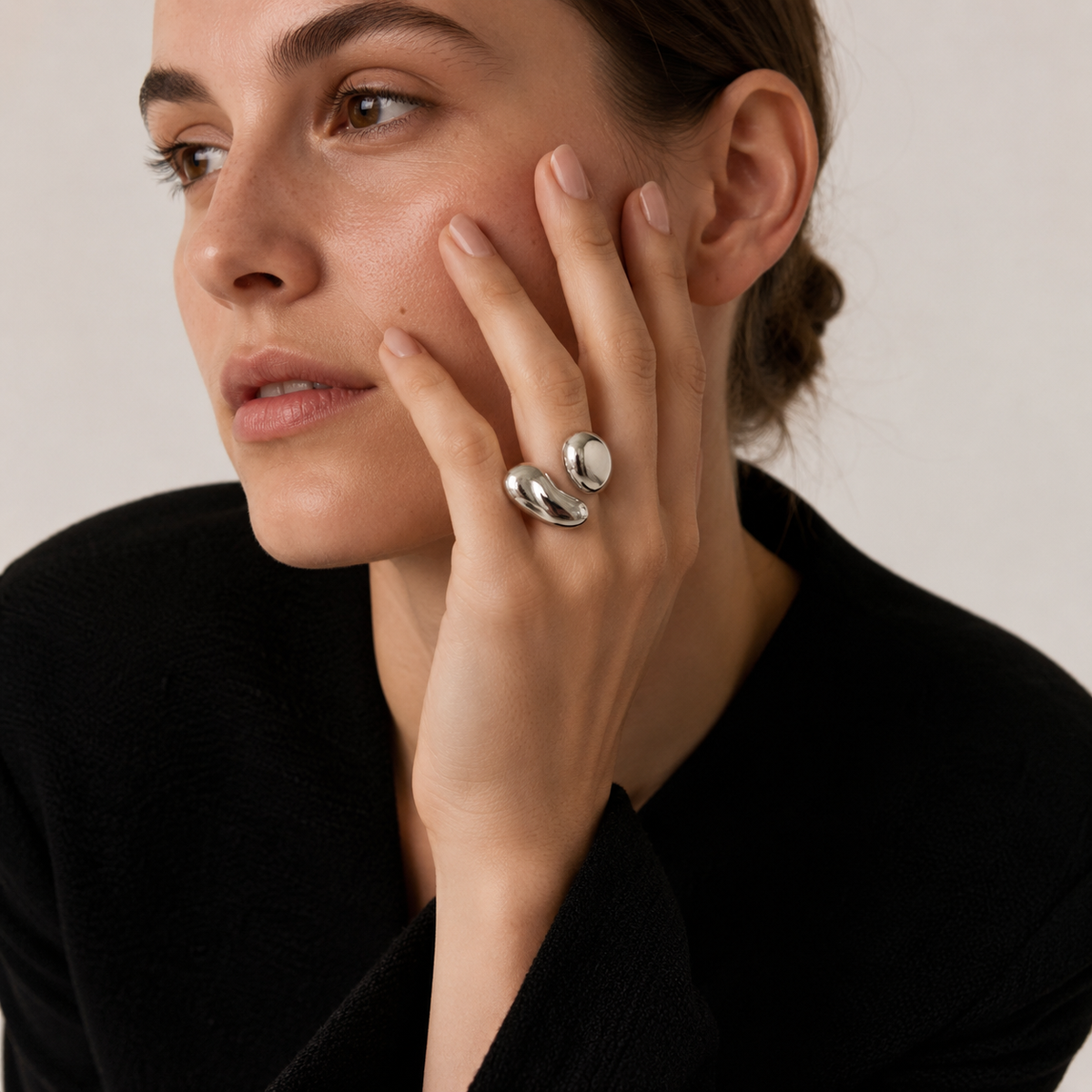 Model wears the silver Côte d'Été RING's two glossy teardrop domes on her finger, hand raised to her cheek.