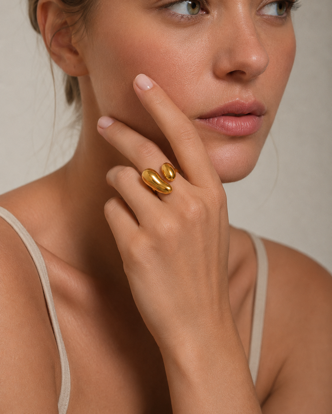 Model wears the gold Côte d'Été RING's two glossy teardrop domes on her finger, hand raised to her chin.