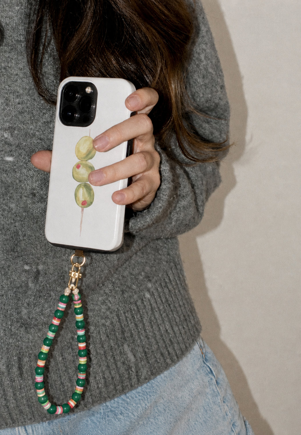 Hand holding a printed phone case with the green beaded Cove SHORT PHONE STRAP attached at the corner.