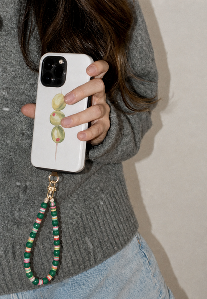 Hand holding a printed phone case with the green beaded Cove SHORT PHONE STRAP attached at the corner.