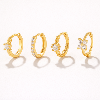 Desiree Set of four gold huggie hoops, each with a different crystal detail: solitaire, pave band, beaded flower, and clover cluster.
