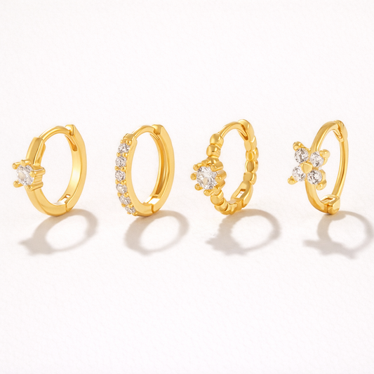 Desiree Set of four gold huggie hoops, each with a different crystal detail: solitaire, pave band, beaded flower, and clover cluster.
