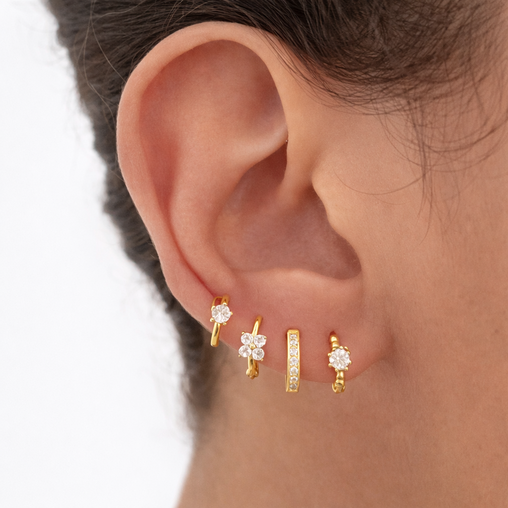 Desiree Set worn stacked along the earlobe, mixing a solitaire hoop, clover cluster, crystal bar stud, and flower hoop.