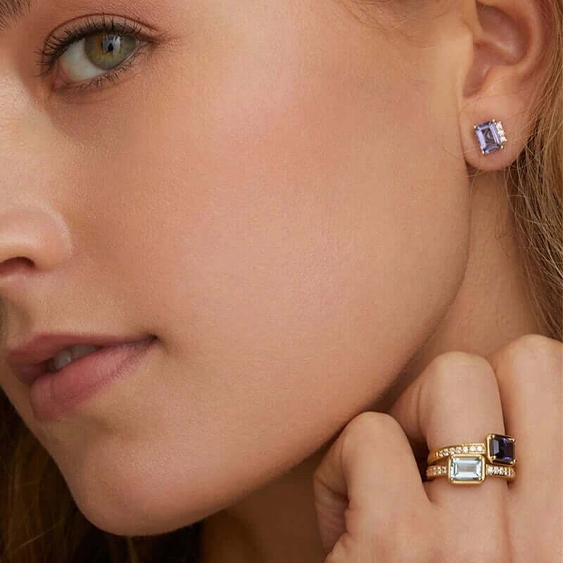 Worn as a stud, Devon Earrings show their emerald-cut purple stone glinting at the earlobe with matching rings nearby.