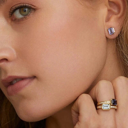 Worn as a stud, Devon Earrings show their emerald-cut purple stone glinting at the earlobe with matching rings nearby.