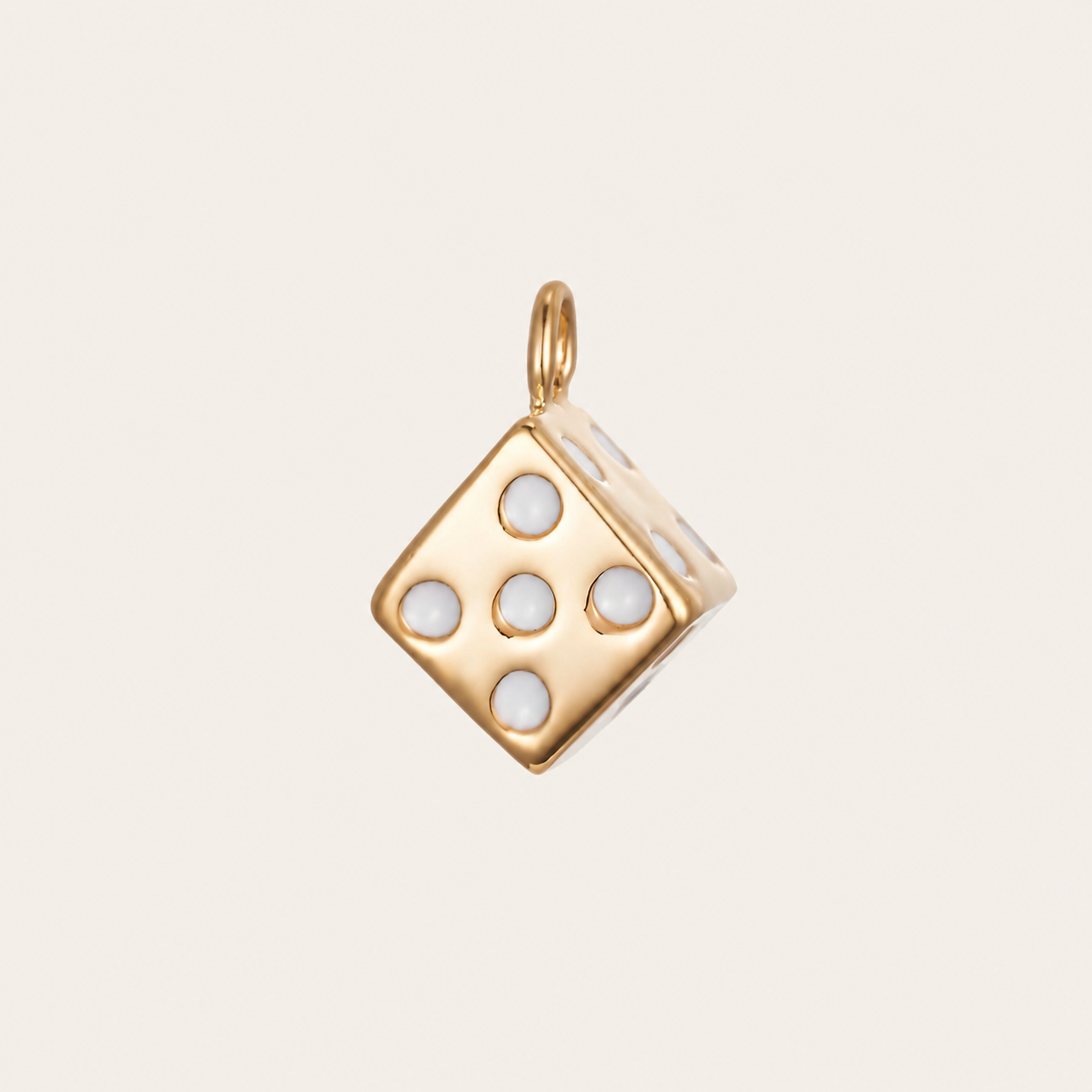 The Dice CHARM in gold, a cube-shaped pendant set with white enamel pips, shown in close-up studio photography on cream.