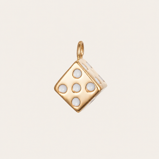 The Dice CHARM in gold, a cube-shaped pendant set with white enamel pips, shown in close-up studio photography on cream.