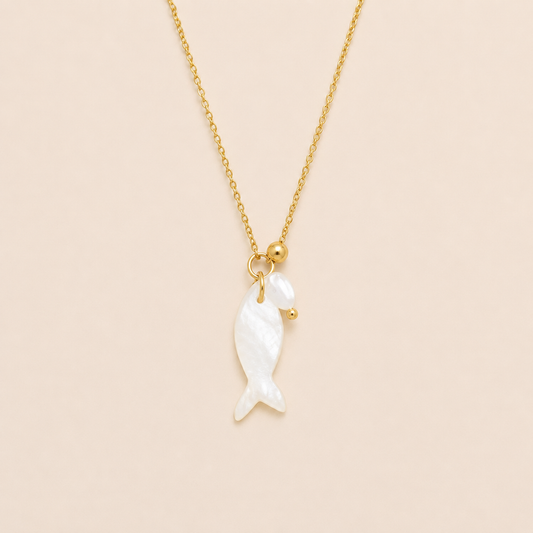 Gold chain necklace with a mother-of-pearl fish charm from the Dolce NECKLACE design, laid flat on a beige background.