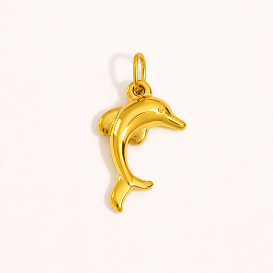 The Dolphin CHARM in a studio flat lay, a polished gold pendant shaped like a leaping dolphin on a cream background.