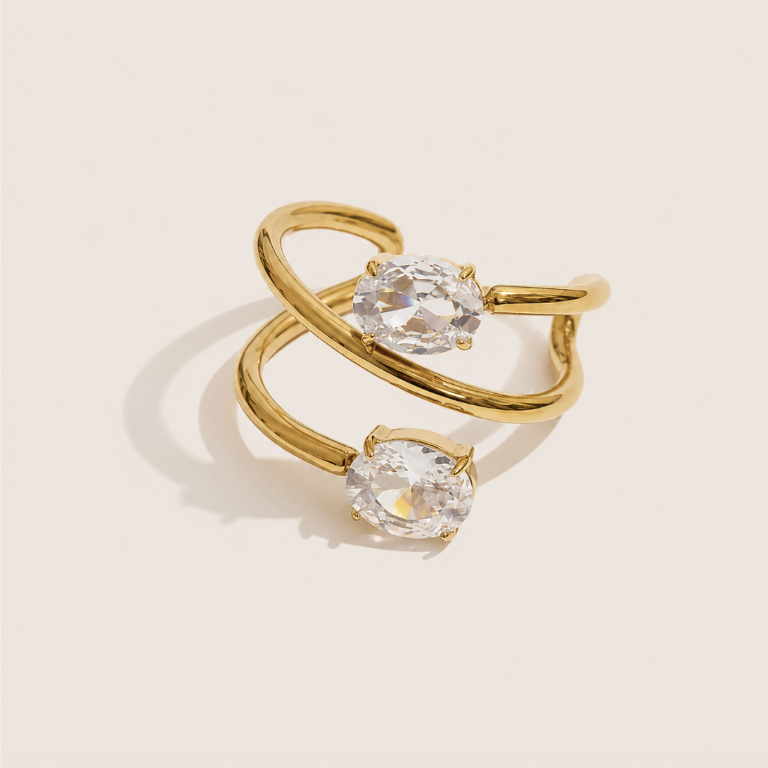 Gold open double-band ring with two prong-set oval white zirconia stones on a cream backdrop — Folie à Trois Double Take RING