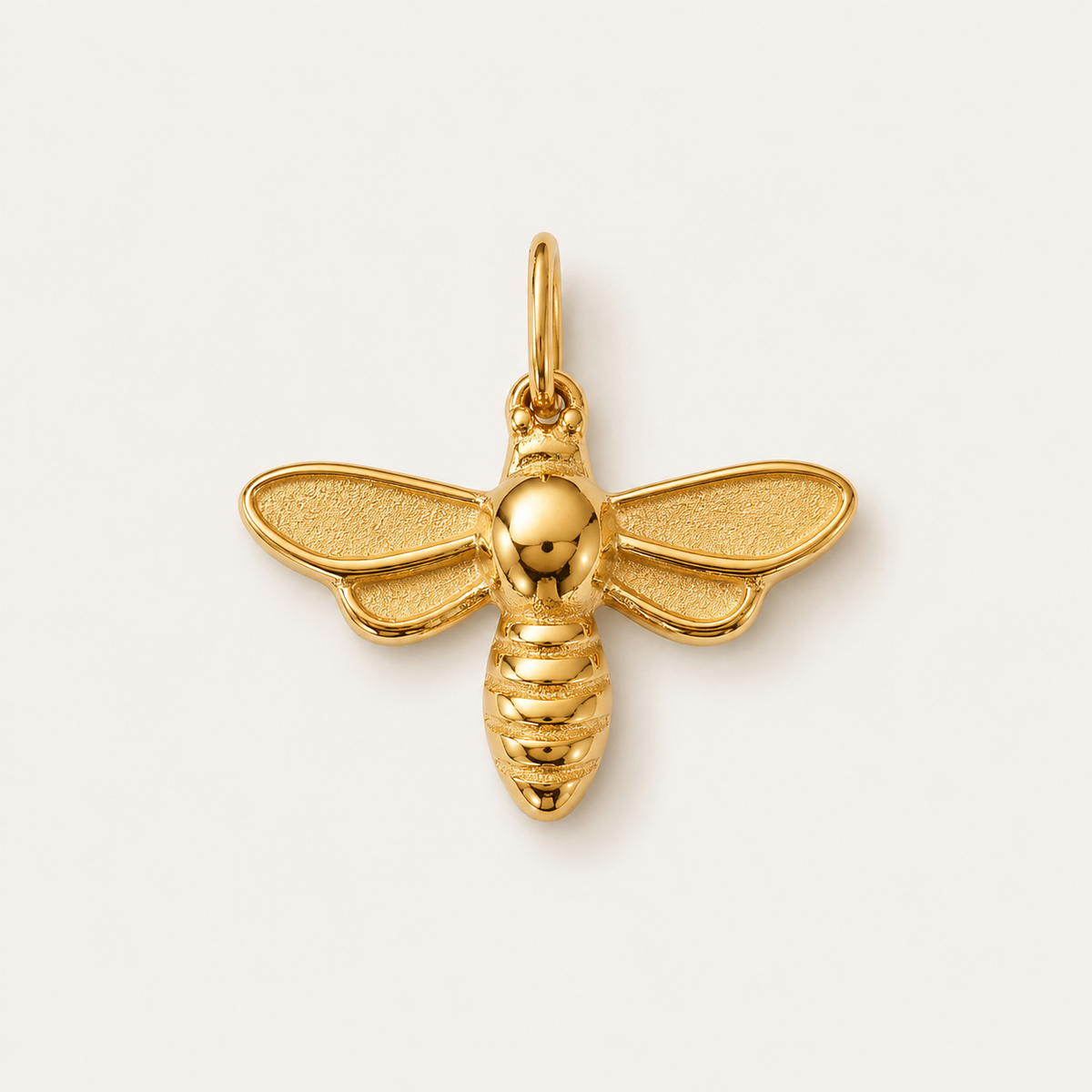The Dragonfly CHARM in gold, a bee-shaped pendant with textured wings and a ribbed body, shown in close-up studio photography.