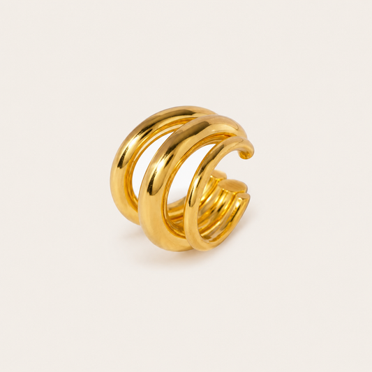 The Dréa EAR CUFF in a studio flat lay, a chunky gold multi-band cuff with three thick stacked rings on cream.