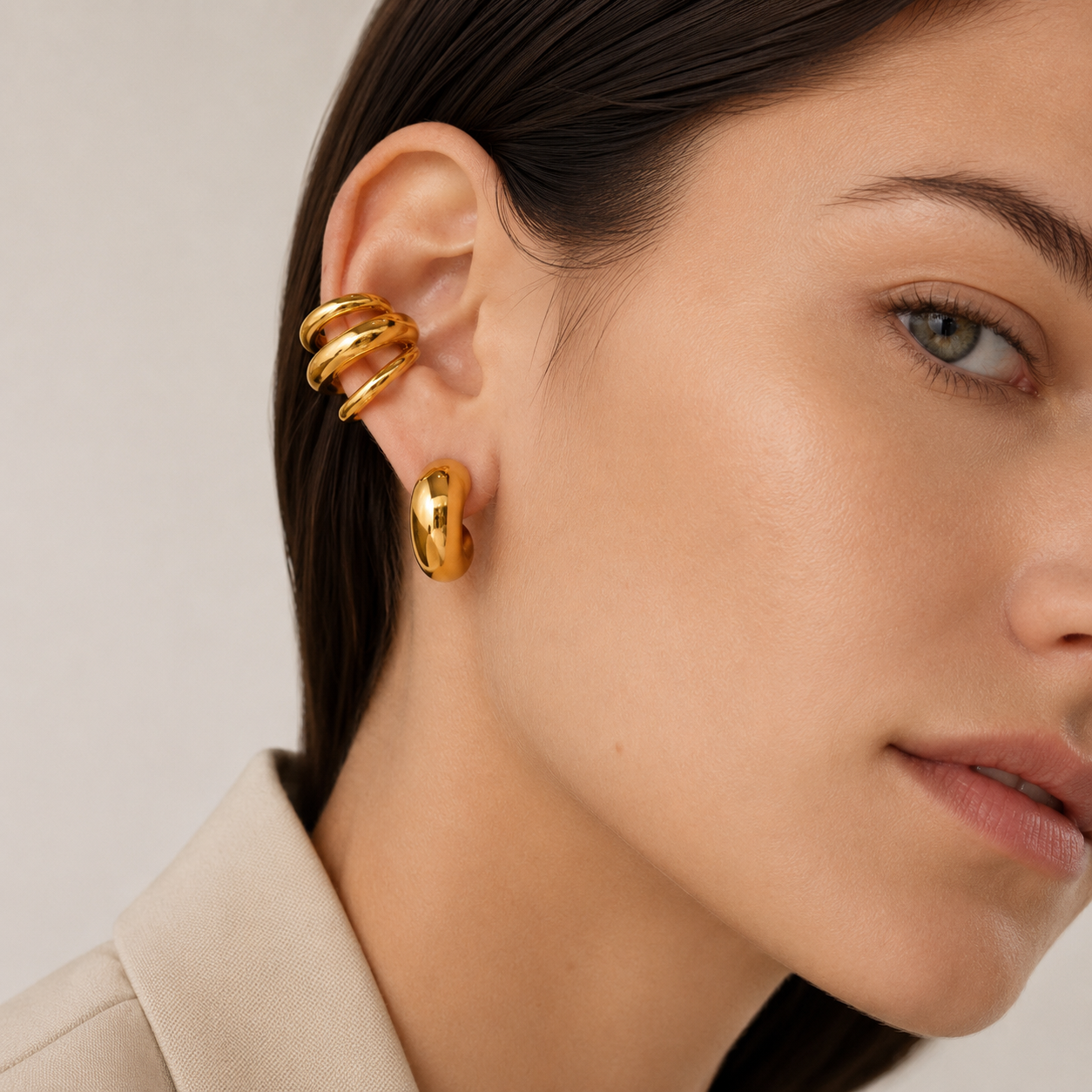 The Dréa EAR CUFF worn on the ear cartilage in close-up, a multi-band gold cuff above a chunky gold hoop earring.