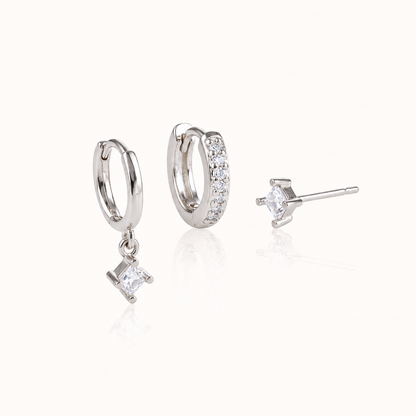 Three silver Eira SET pieces: a huggie with a square crystal drop, a pavé huggie hoop and a square crystal stud, on white.