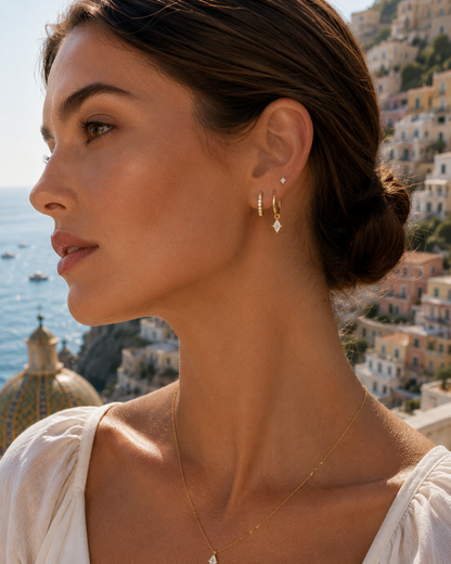 Eira Set worn as an ear stack with a pave hoop and diamond-drop huggie, styled outdoors against a coastal Amalfi backdrop.