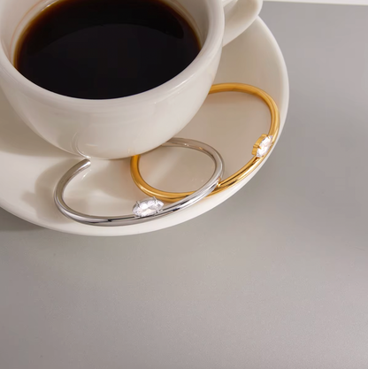 Electric Frost BRACELET pair in gold and silver resting on a saucer beside a cup of coffee, styled flat lay.