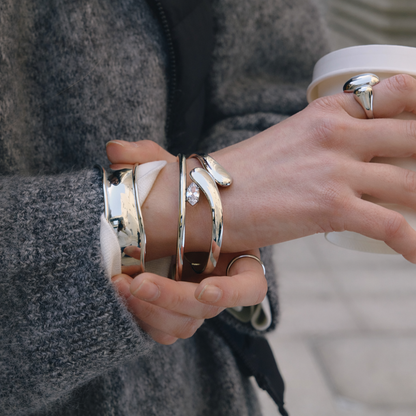 Electric Frost BRACELET in silver worn stacked with other silver cuffs and rings, model in a wool coat outdoors.