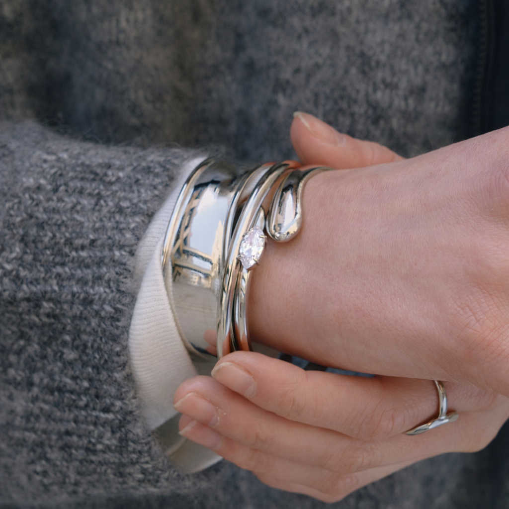 Electric Frost BRACELET in silver worn stacked with other silver cuffs, close-up of clasped hands and rings.