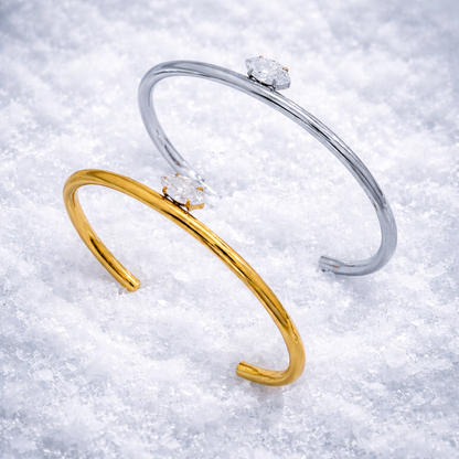 Electric Frost BRACELET pair in gold and silver, open cuffs with marquise crystals, resting on fresh snow.