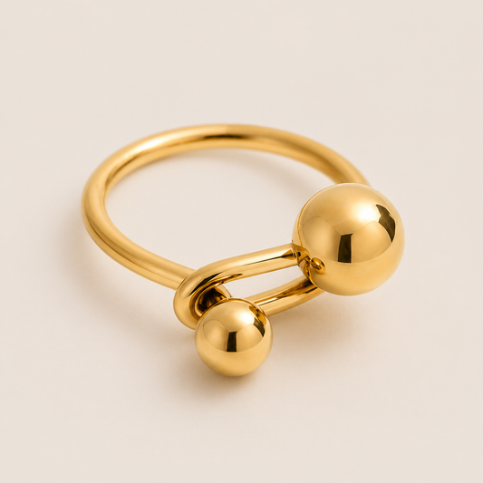 Gold bypass ring with two polished balls of different sizes facing each other across an open band — Folie à Trois Electric Love RING.