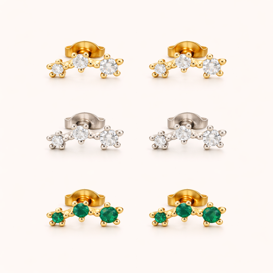Three-stone climber earrings shown together in gold, silver, and emerald-green colorways, each set with a graduated row of round stones.
