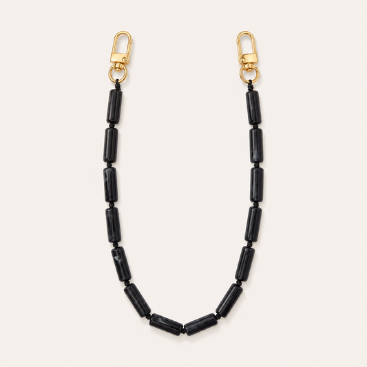 Black tube-bead phone chain with gold lobster clasps laid flat on cream — Folie à Trois Elowen wholesale phone chain