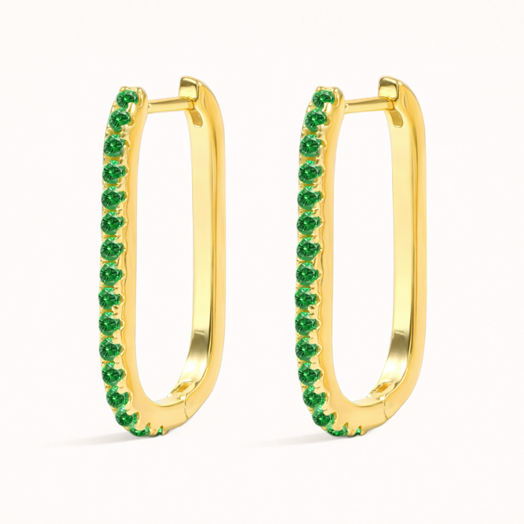 Fair Game Earrings show off their oblong hoop silhouette in gold, the edge set with a row of sparkling green pave stones.