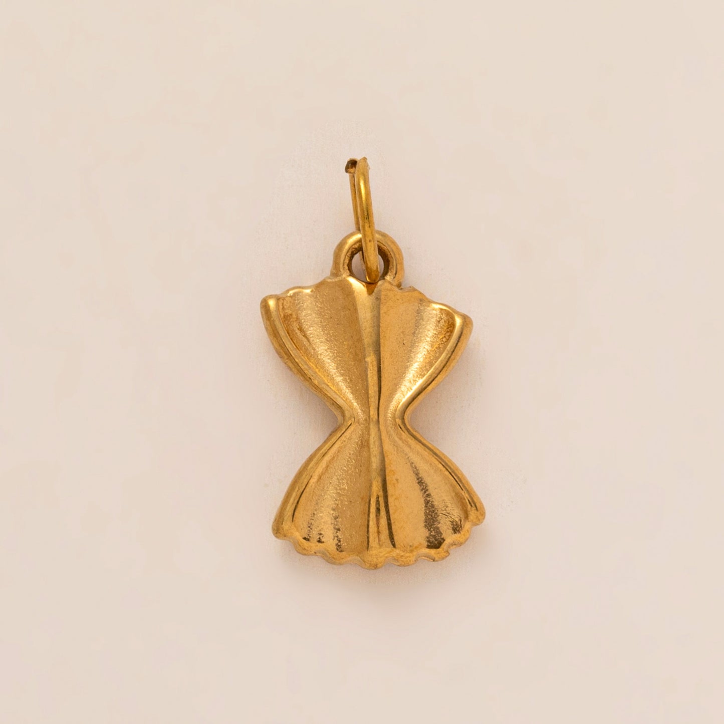 The Farfalle Pasta CHARM in gold, a bow-shaped pasta pendant with fluted edges, shown in close-up studio photography on cream.