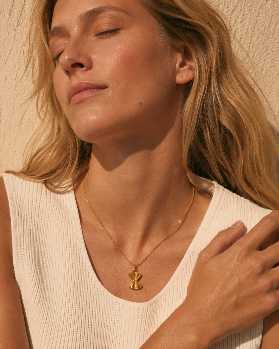 The Farfalle Pasta CHARM worn as a pendant on a fine gold chain necklace, resting at the neckline over a cream ribbed top.