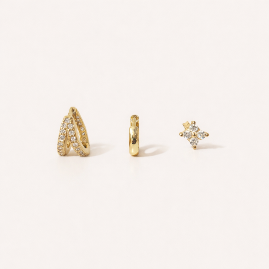 Faye Set of gold jewelry, a pave crossover hoop, a plain huggie hoop, and a four-point crystal stud, laid flat.
