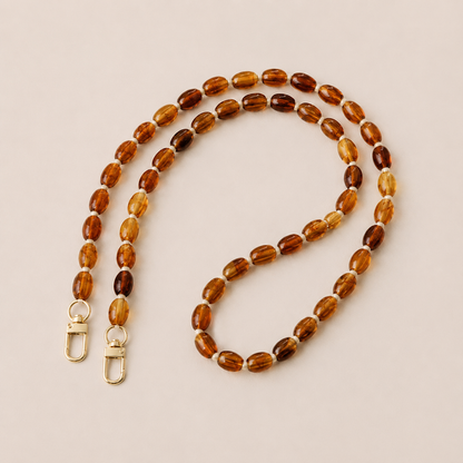 Folie à Trois Fennel long wholesale phone chain in amber oval beads with cream spacers and gold clasps, laid flat on a cream background.