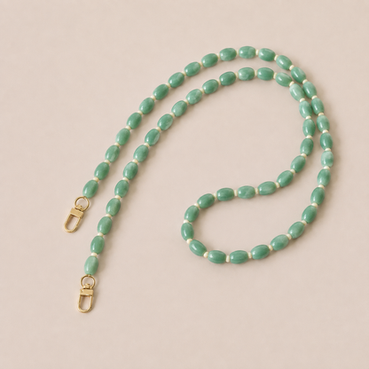 Folie à Trois Fennel long wholesale phone chain in jade green oval beads with cream spacers and gold clasps, laid flat on a cream background.