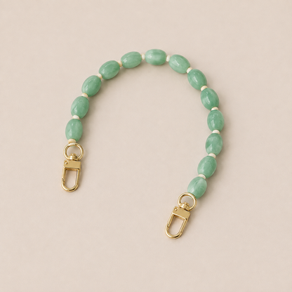 Folie à Trois Fennel short wholesale phone chain in jade green oval beads with cream spacers and gold clasps, laid flat on a cream background.