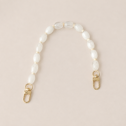 Folie à Trois Fennel short wholesale phone chain in white oval beads with cream spacers and gold clasps, laid flat on a cream background.