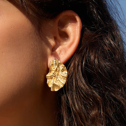 Gold Feuille EARRING, a textured ruffled leaf stud, worn by a model with wavy dark hair in the sun — Folie à Trois