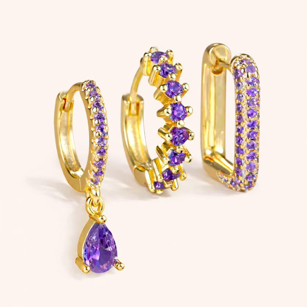 The Fia SET is shown in a purple crystal colorway across its drop huggie, zigzag hoop, and pave rectangle hoop.
