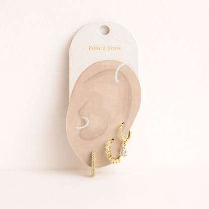 The Fia SET is displayed on a branded card shaped like an ear, showing the gold pieces and teardrop charm.
