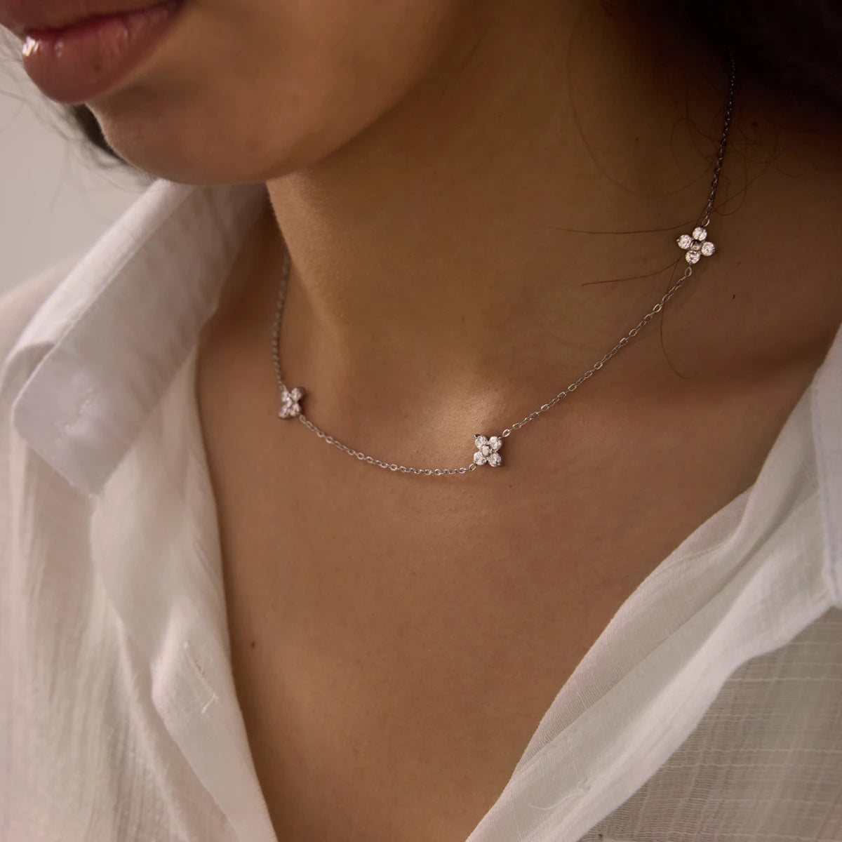 Fiore NECKLACE with delicate zirconia flower stations worn with an open white shirt — Folie à Trois wholesale jewelry