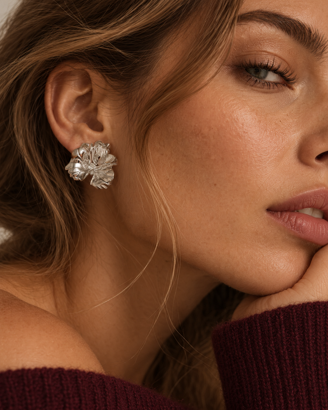 Close-up of silver-tone Fleurette EARRINGS, a bold sculpted flower stud, on a model in a burgundy off-shoulder knit