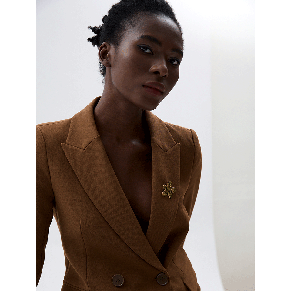 Model wears a gold Flora BROOCH pinned to the lapel of a brown blazer — Folie à Trois wholesale jewelry